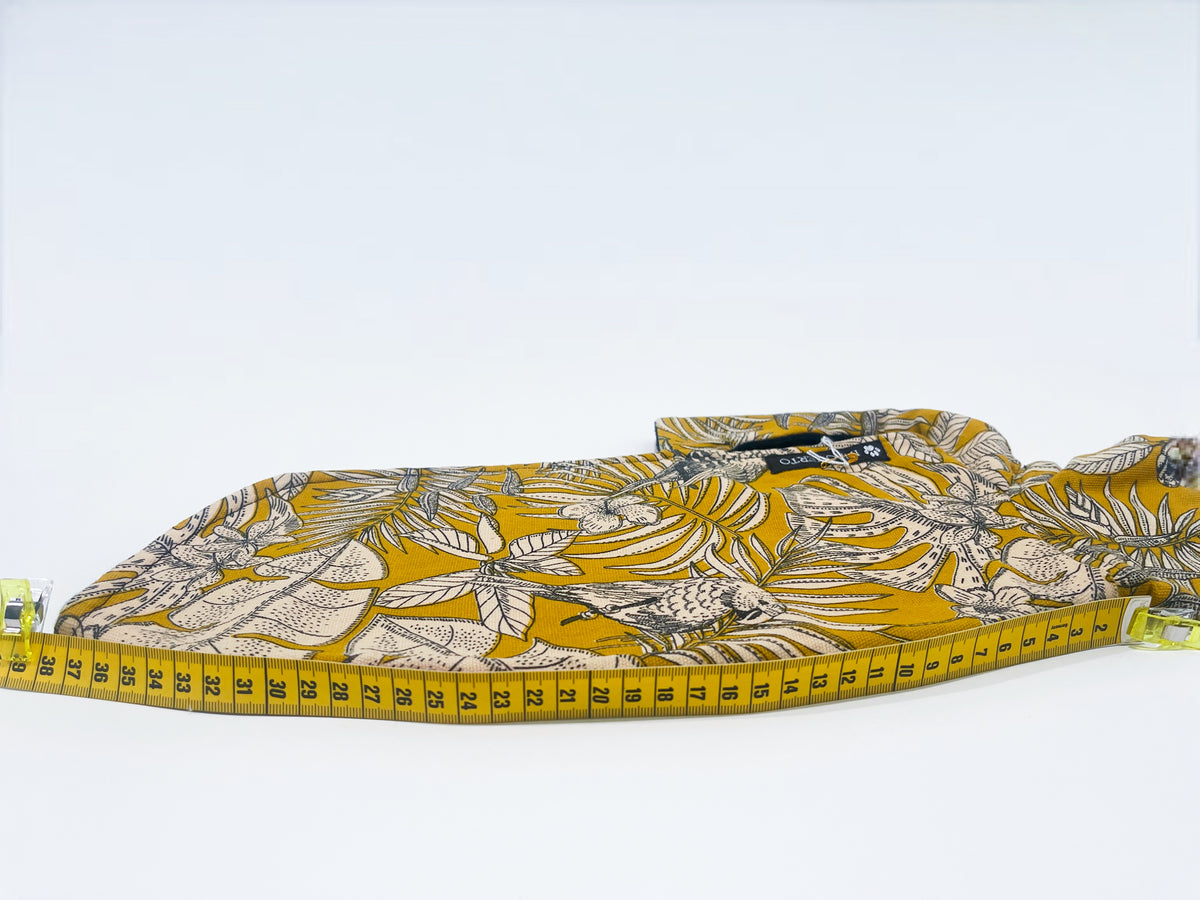 Manteau moutarde à motifs de perroquets INnOVERTO Dog, photographié à plat avec un mètre indiquant la longueur du dos.